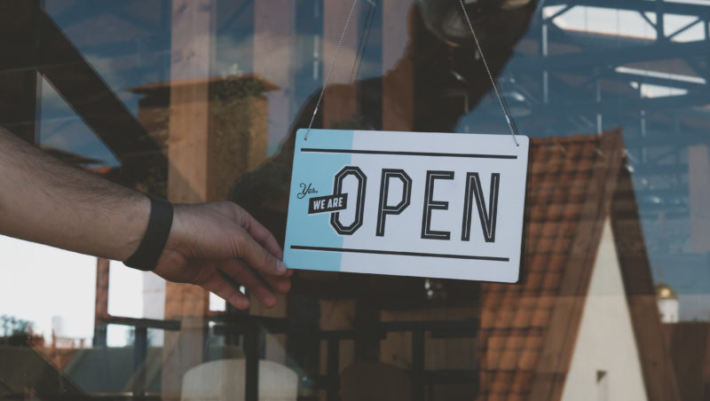 Caucasian male turning sign from closed to open on the entrance door of his small cafe. 