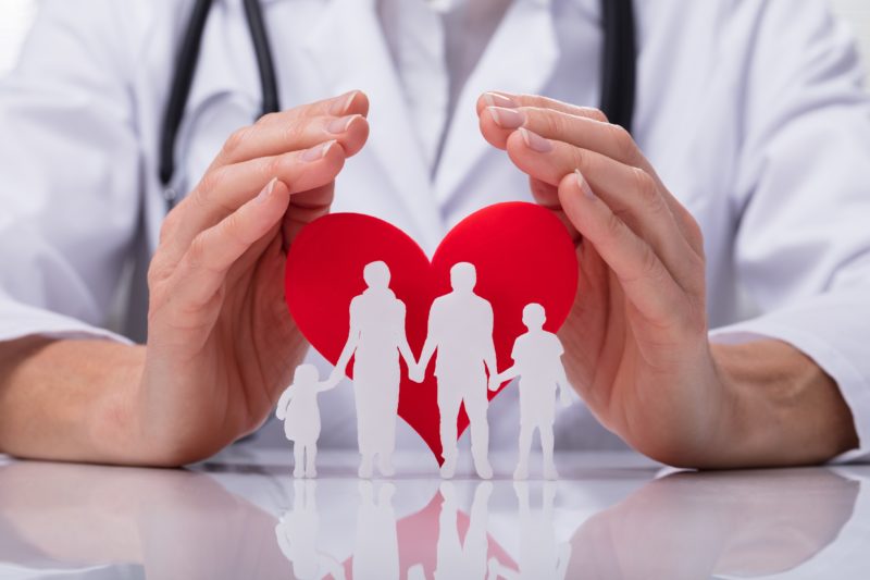 Close-up Of A Doctor's Hand Protecting Family Cut Out With Red Heart Shape