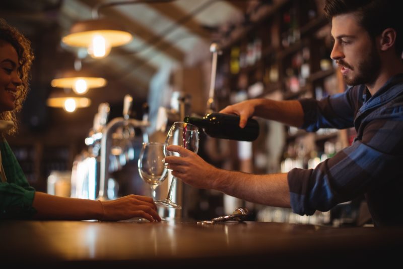 Male bar tender pouring wine in glasses